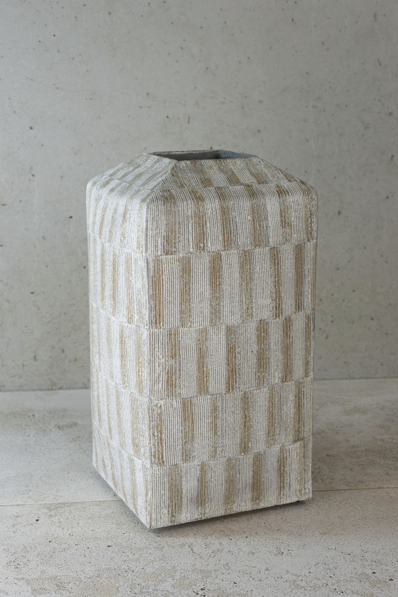 Quadratische hohe Vase mit kleiner Öffnung in alterneierenden weiß-beigen Rechteckfeldern dekoriert, in grauem Umraum.