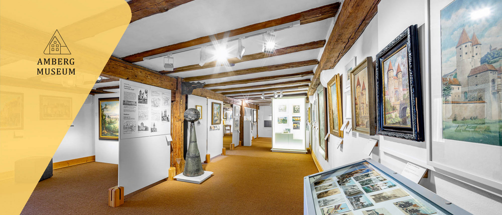 Ausstellungsraum mit vielen Gemälden mit Stadtansichten von Amberg.