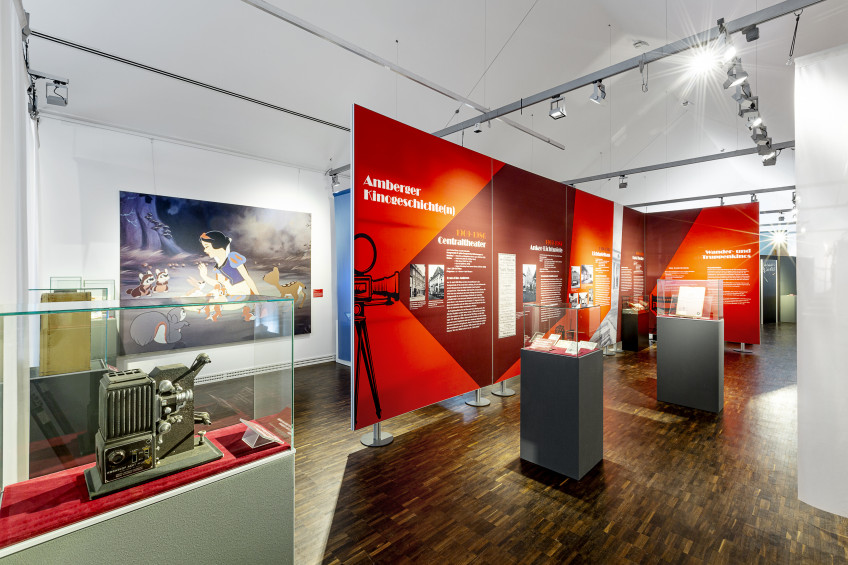 Vitrinen mit Glashauben und hohe Textilspannwände im Ausstellungsraum.