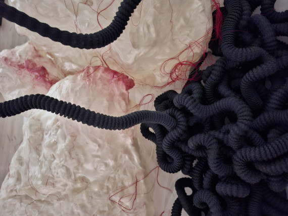 Ausschnitt einer Installation aus roten F&auml;den, schwarz-gerillten Schl&auml;uchen und beigem Gewebe